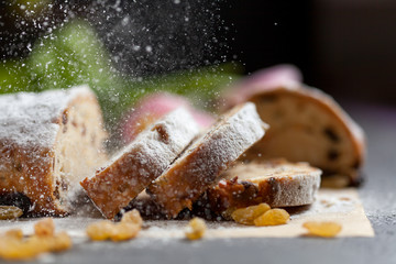 freshly baked cake with sweets, raisins and candied fruits, sprinkled with powdered sugar on a gray table with pink tulips