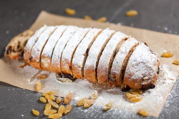 freshly baked cake with sweets, raisins and candied fruits, sprinkled with powdered sugar on a gray table