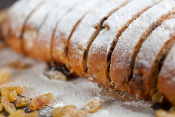 freshly baked cake with sweets, raisins and candied fruits, sprinkled with powdered sugar on a gray table