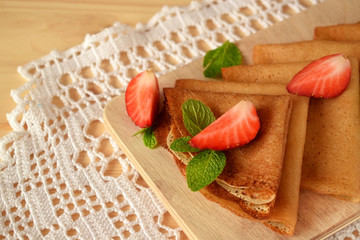 Fototapeta na wymiar Golden crepes with fresh strawberries and mint on a wooden board