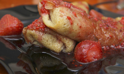 Rolled up pancakes filled by cottage cheese and strawberry jam over with berries