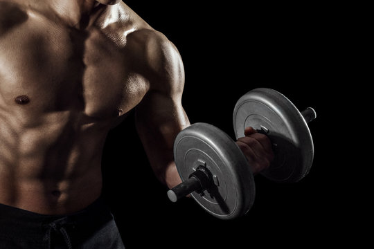 Highly retouched fitness model and bodybuilder training with dumbbells. posing the biceps and shoulder. concept of strength and power. black background.