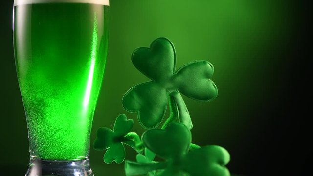 St. Patric's Day green beer pouring over dark green background, decorated with shamrock leaves. Pint of Green beer close-up. Glass of beer for Patric Day pub celebration 4K UHD video