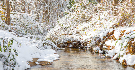 A wintry scene with a creek and a touch of color from tree foliage on a bright sunny day.  High...