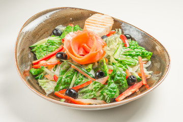 Dietary salad of bell pepper, lettuce, cucumber, olives and olive oil, a slice of bread. In the middle of the dish is a rose flower-of red fish - salmon.
