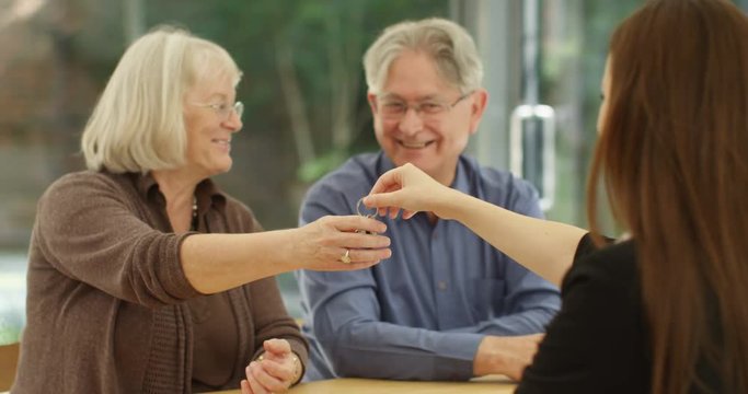 4K Happy senior couple taking key to new home & shaking hands with estate agent. Slow motion