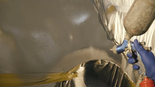 Mechanic spraying primer on a car surface. 4K