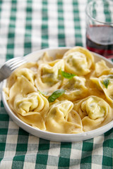 Traditional italian ravioli with ricotta cheese and spinach with a glass of red wine on table covered with green chechered tablecloth