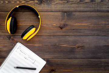 Work desk of modern composer. Music notes near headphones on dark wooden background top view copy...