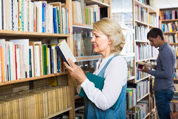 mature woman with book among bookshelves .