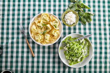 Overhead image of traditional italian ravioli with ricotta cheese and spinach tagliatelle on table covered with green checkered tablecloth