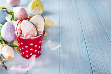Happy Easter gingerbread cookie eggs with bucket and tulips with colorful eggs on blue wood background,
