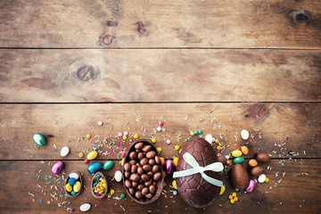 Chocolate Easter eggs on wooden background with ribbon bow and candies. 