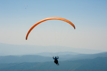 Paraglider flies over a mountain valley on a sunny summer day. Paragliding in the Carpathians in the summer.