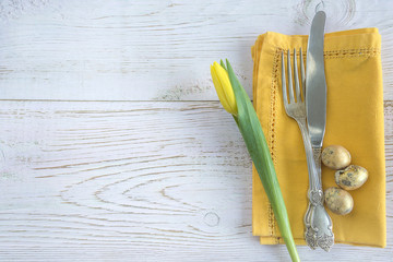 Festive place setting with yellow napkin, tulip and quail eggs