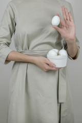 Unrecognizable woman in grey dress holding white eggs preparing for Easter holiday.
