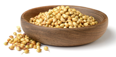dried coriander seeds in the wooden plate, isolated on white