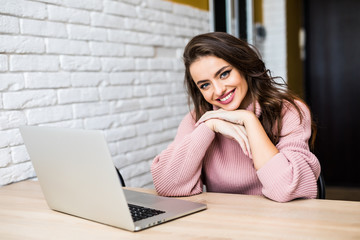 Happy casual beautiful woman working on a laptop sitting at table in the house.