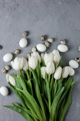 A bouquet of white tulips and chicken and quail eggs on a gray concrete background. Top view. Flat lay. Postcard for Easter and Spring Holidays.