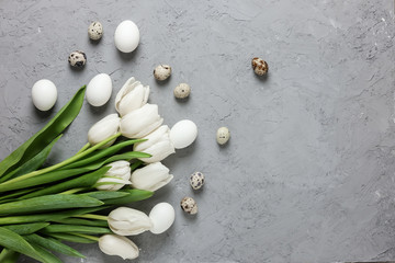 A bouquet of white tulips and chicken and quail eggs on a gray concrete background. Top view. Flat lay. Postcard for Easter and Spring Holidays.