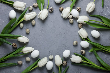 A circle of white tulips and chicken and quail eggs on a gray concrete background. Top view. Flat lay. Postcard for Easter and Spring Holidays.