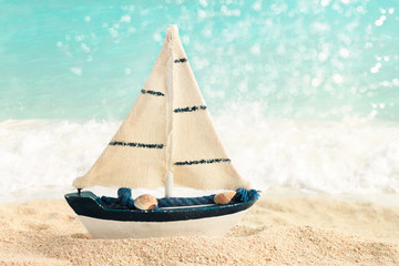 
Toy sail boat on sand shore with sparkling light blue sea background. Beach vacation, dreaming...