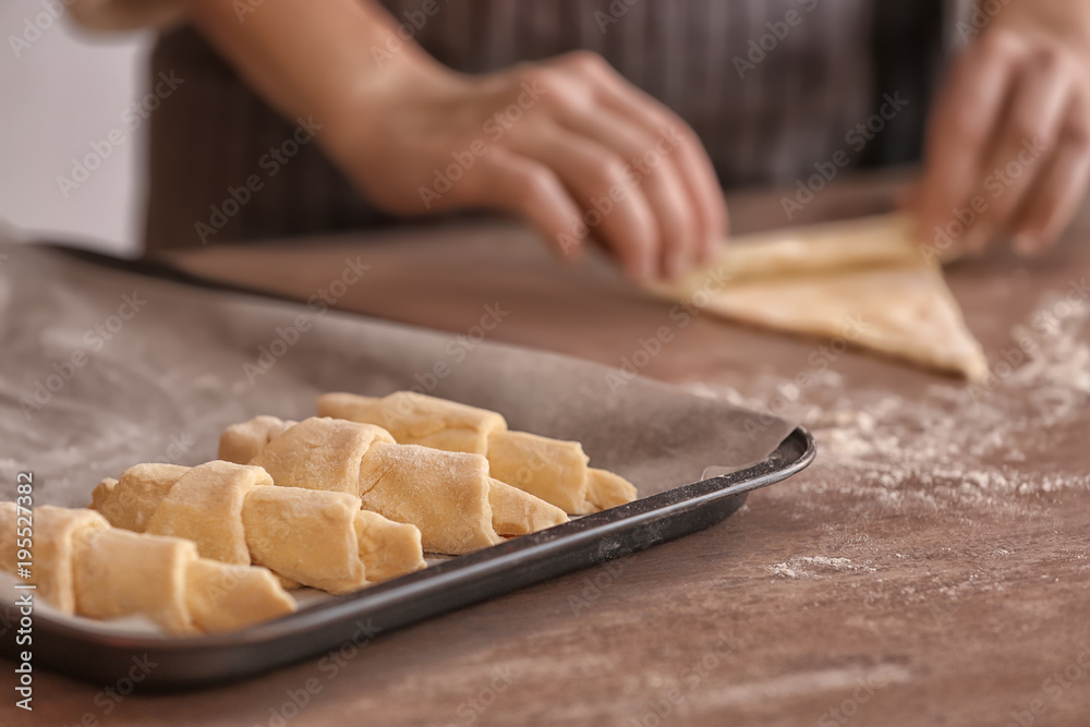 Sticker baking sheet with raw croissants and blurred woman on background