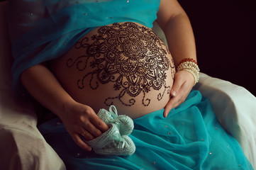 Mehendi artist paints an ornament of mandala with henna on an pregnancy woman’s belly