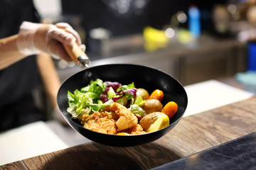 Chef holding frying pan with delicious fish fillets and vegetables in restaurant kitchen