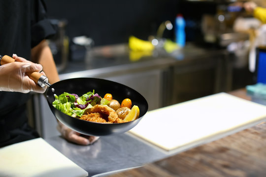 Chef holding frying pan with delicious fish fillets and vegetables in restaurant kitchen
