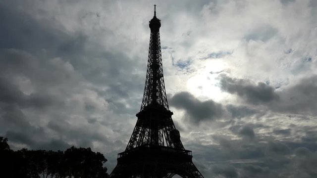 A rough view of the famous Eiffel Tower in cloudy weather with rampant and fluffy grey and white clouds at gloomy sunset
