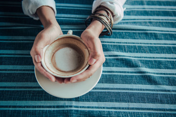 Asian woman  hands holding cup of coffee on  table.Focus on the coffee cup