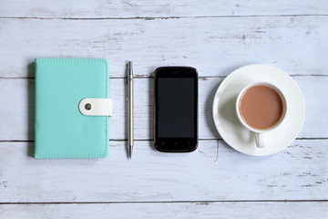 Top view of notebook,pen,smartphone and a cup of coffee on white wooden background.