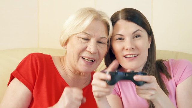 Mother and daughter gamers playing video games at home. Addicted senior and teen players with remote controller of game console. Cybersport for active modern elderly people