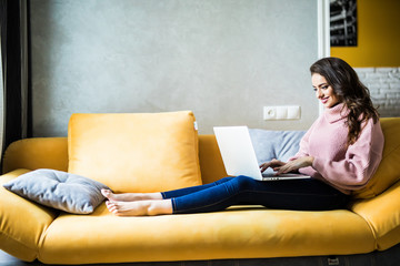 Happy woman sitting on couch using her laptop in the living room at home