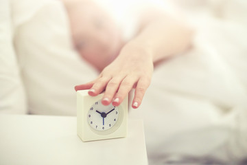 close up of woman with alarm clock in bed at home