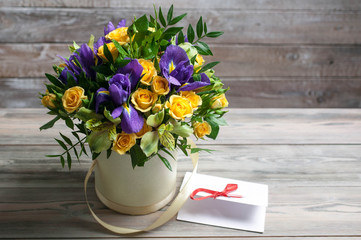 Bouquet from irises and a rose in a gift box on a wooden background