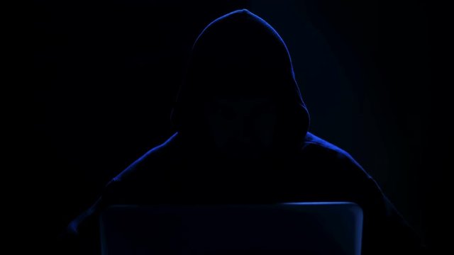 portrait of  hooded hacker working on a computer in the dark 