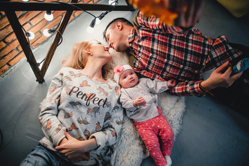 mom, dad and baby lie on a woolen carpet and smile