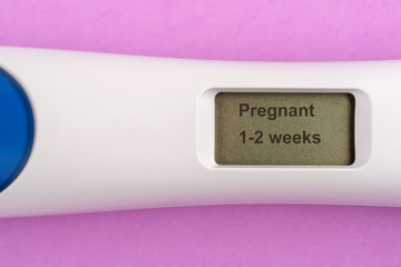 Modern electronic pregnancy test with positive results on pink background.