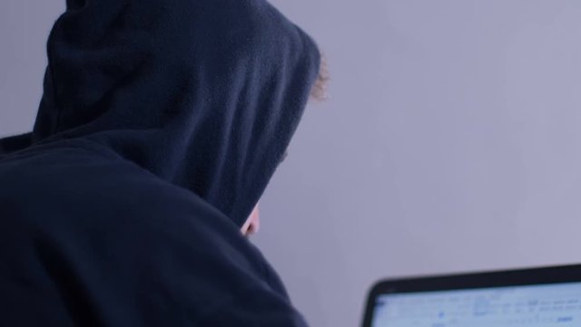 focus on Hacker in hood cracking code using laptop in a room
