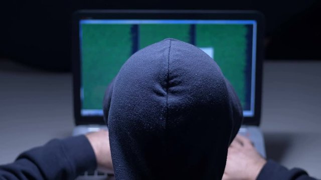 Hacker in hood cracking code using laptop in a room