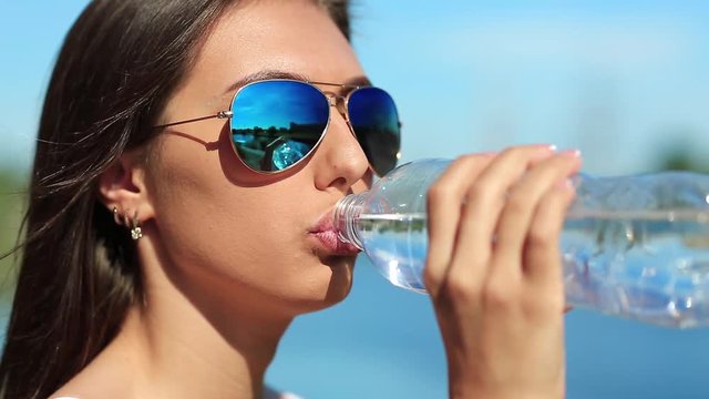 Girl in blue sun glasses drinks water. Attractive woman in sunglasses drinks clean water from a bottle