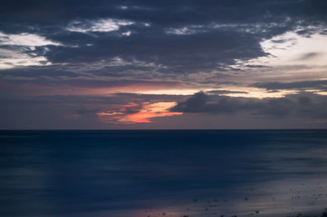 A long exposure of the sea at blue hour, as dawn starts to break over a sandy beach.