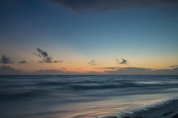 Fototapeta na wymiar A long exposure of the sea at golden hour, as dawn starts to break over a white sandy beach.