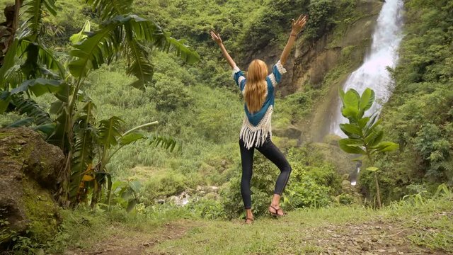 Young caucasian woman raising hands at Kebumen waterfall in Java, Indonesia