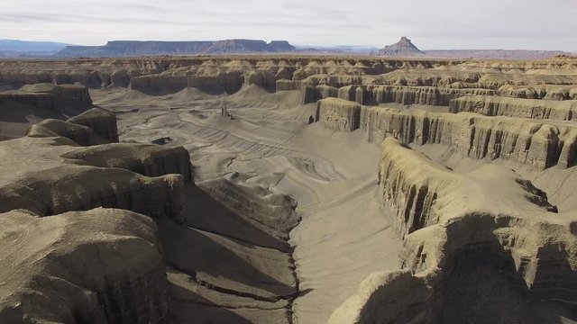 Aerial view flying backwards over maze of cliffs in the desert revealing valley at the base in the Utah desert.