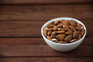 A lot of almonds in a white plate on a wooden table.