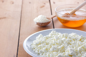 Cheese, fresh cottage cheese in a white plate, wooden spoon, cottage cheese and honey on a wooden background, sour cream in a wooden spoon, dairy products on a natural background, retro style