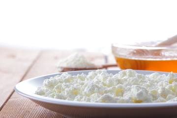 Cheese, fresh cottage cheese in a white plate, wooden spoon, cottage cheese and honey on a wooden background, sour cream in a wooden spoon, dairy products on a natural background, retro style